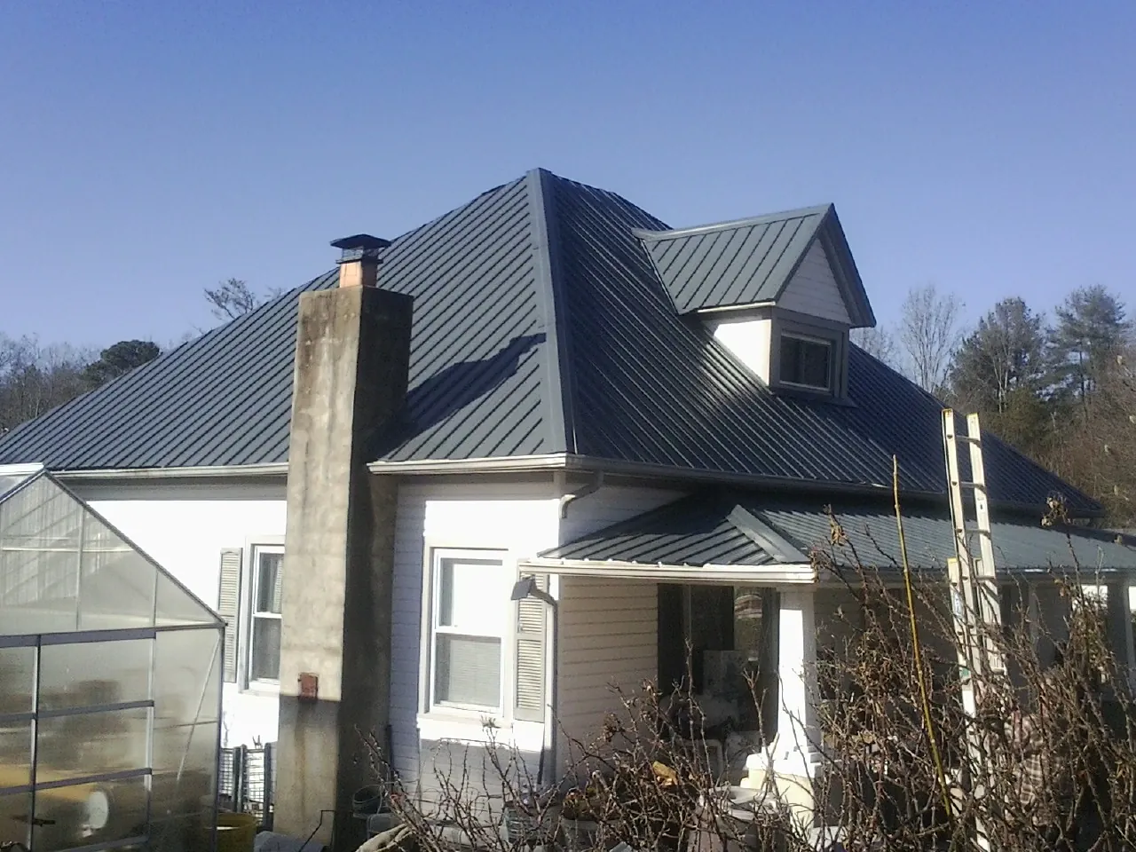 Dark blue standing seam metal roof on a white farmhouse with dormer — Slate & Tile Roof Repair by Roofing Brothers in Oakland Gardens