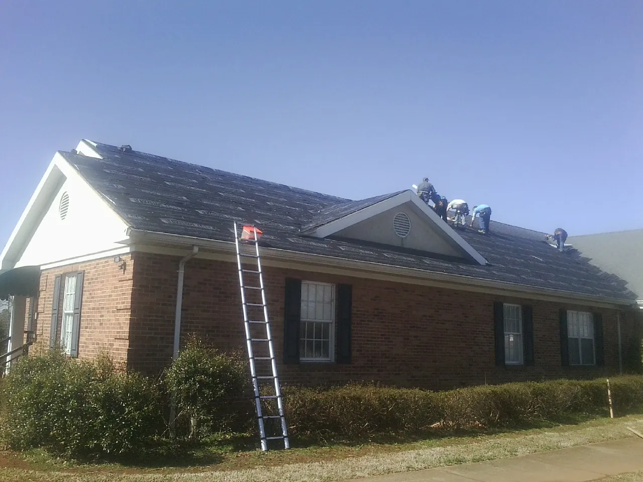 Crew tearing shingles off a brick ranch roof with a ladder set — Metal Roof Repair work by our crew in Oakland Gardens