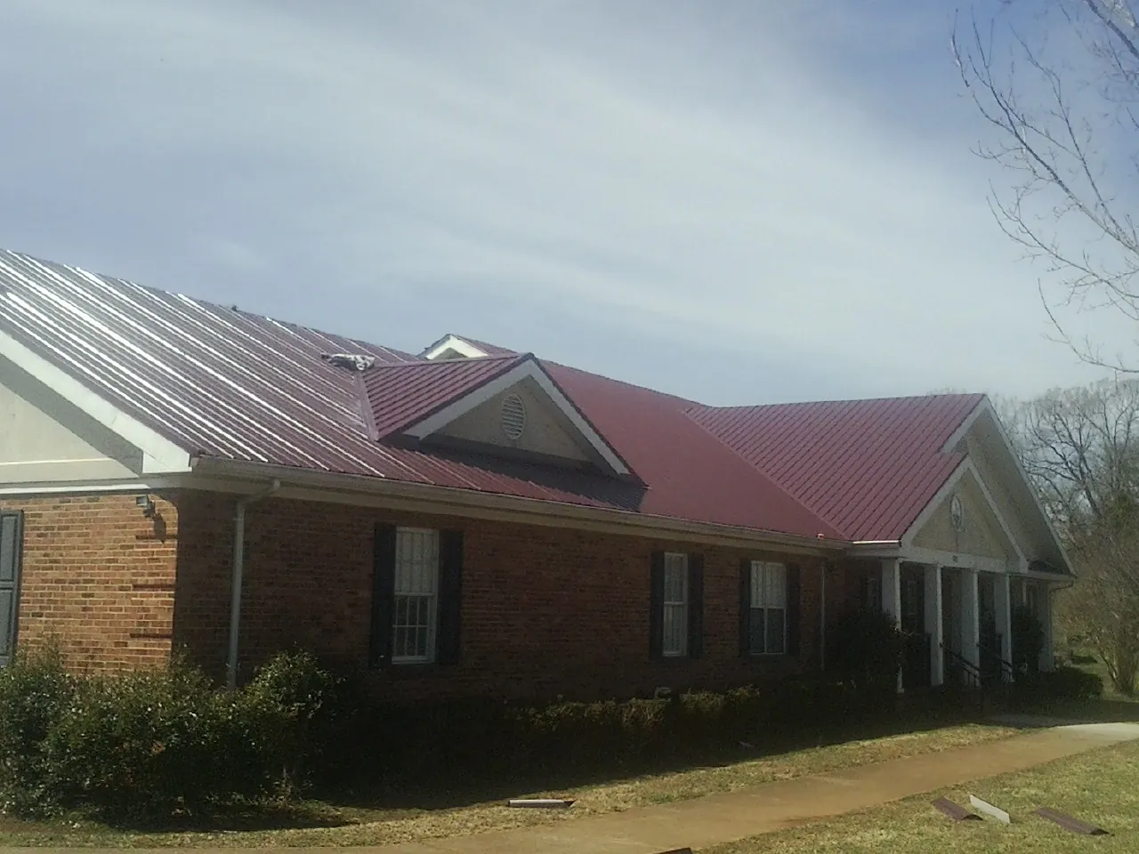 Red metal roof with gabled entries on a long brick building, from a Hail Damage Roof Repair job in Oakland Gardens