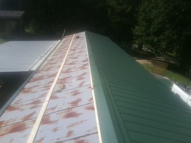 Old rusted panels beside newly installed green metal roofing — Wind Damage Roof Repair by Roofing Brothers in Oakland Gardens