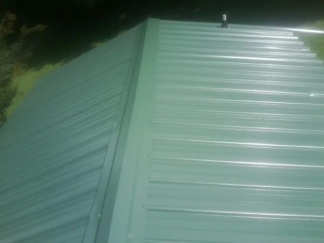 New green metal panels meeting at the ridge of a roof — Flat Roof Repair work by our crew in Oakland Gardens