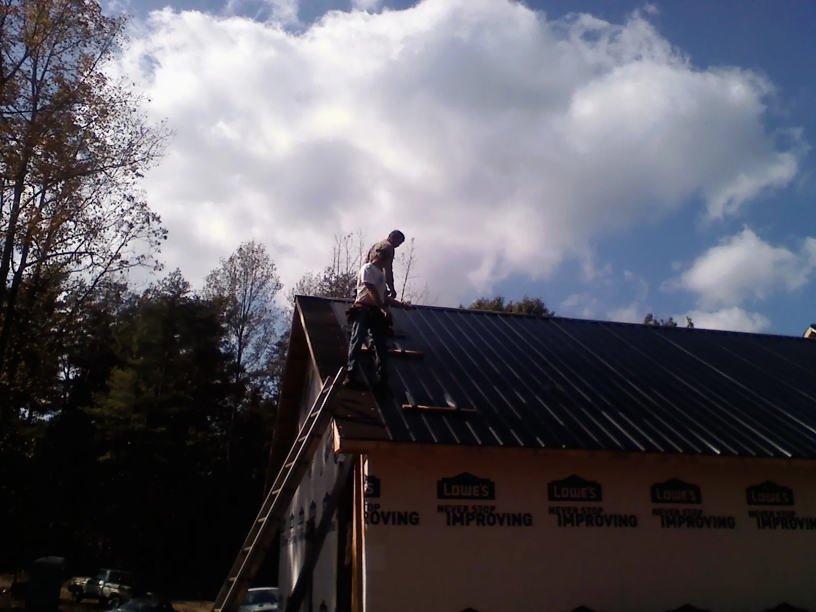 Roofer fastening dark metal panels high against a cloudy sky, from a Roof Inspection job in Oakland Gardens