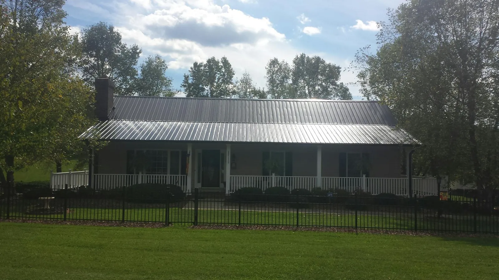 Gray metal roof on a brick ranch with a full width front porch — Gutter Guard Installation work by our crew in Oakland Gardens