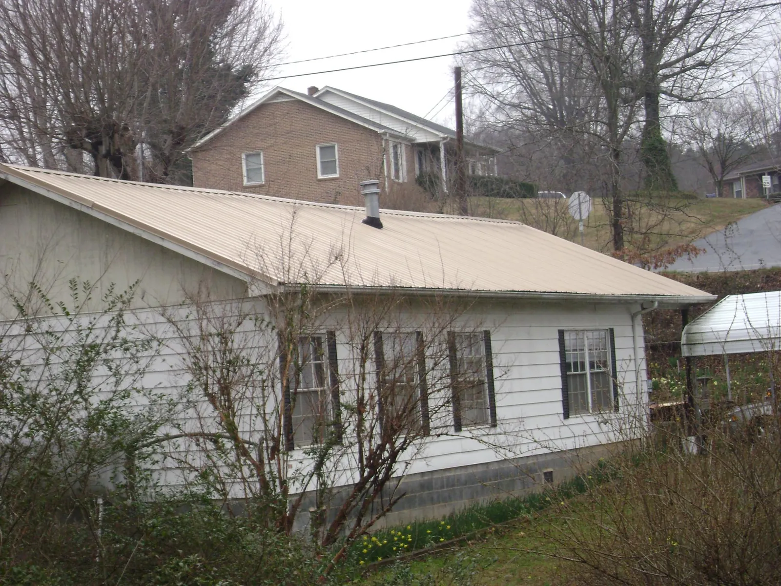 Tan metal roof on a white sided house set into a hillside — Commercial Roofing by Roofing Brothers in Oakland Gardens