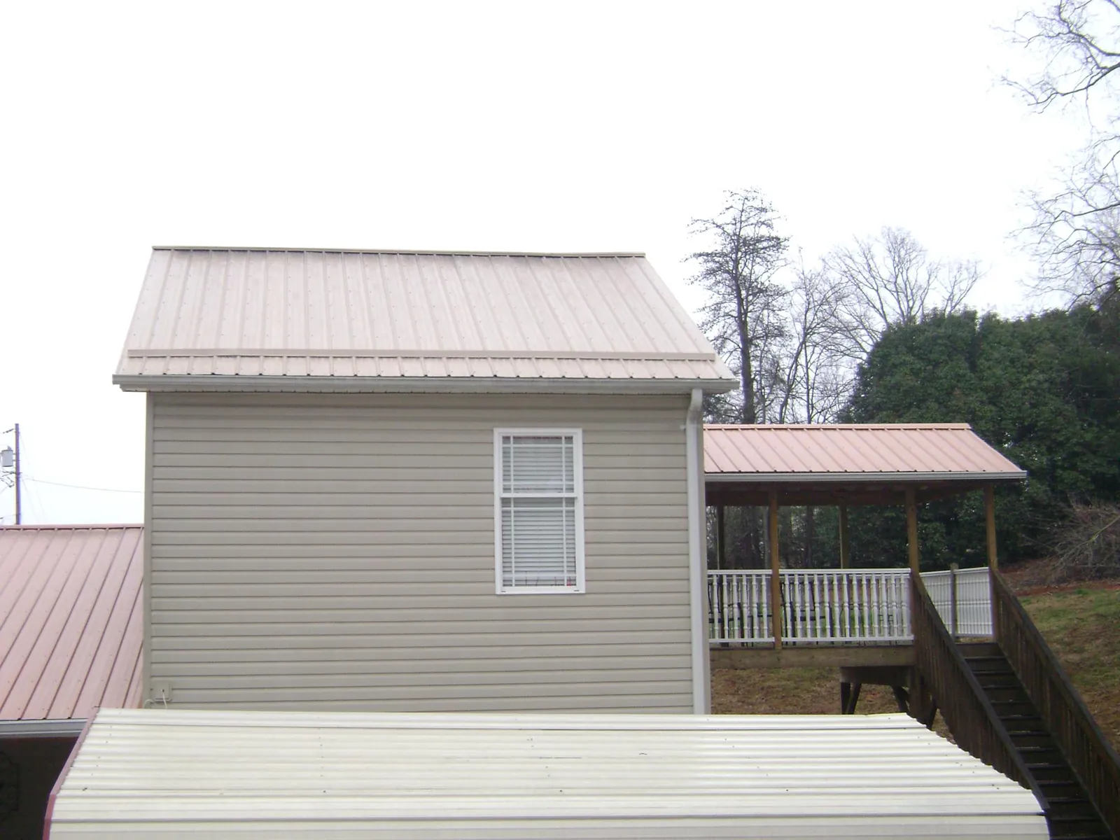 Tan metal roofs on a two story addition and attached porch, from a Roof Replacement job in Oakland Gardens