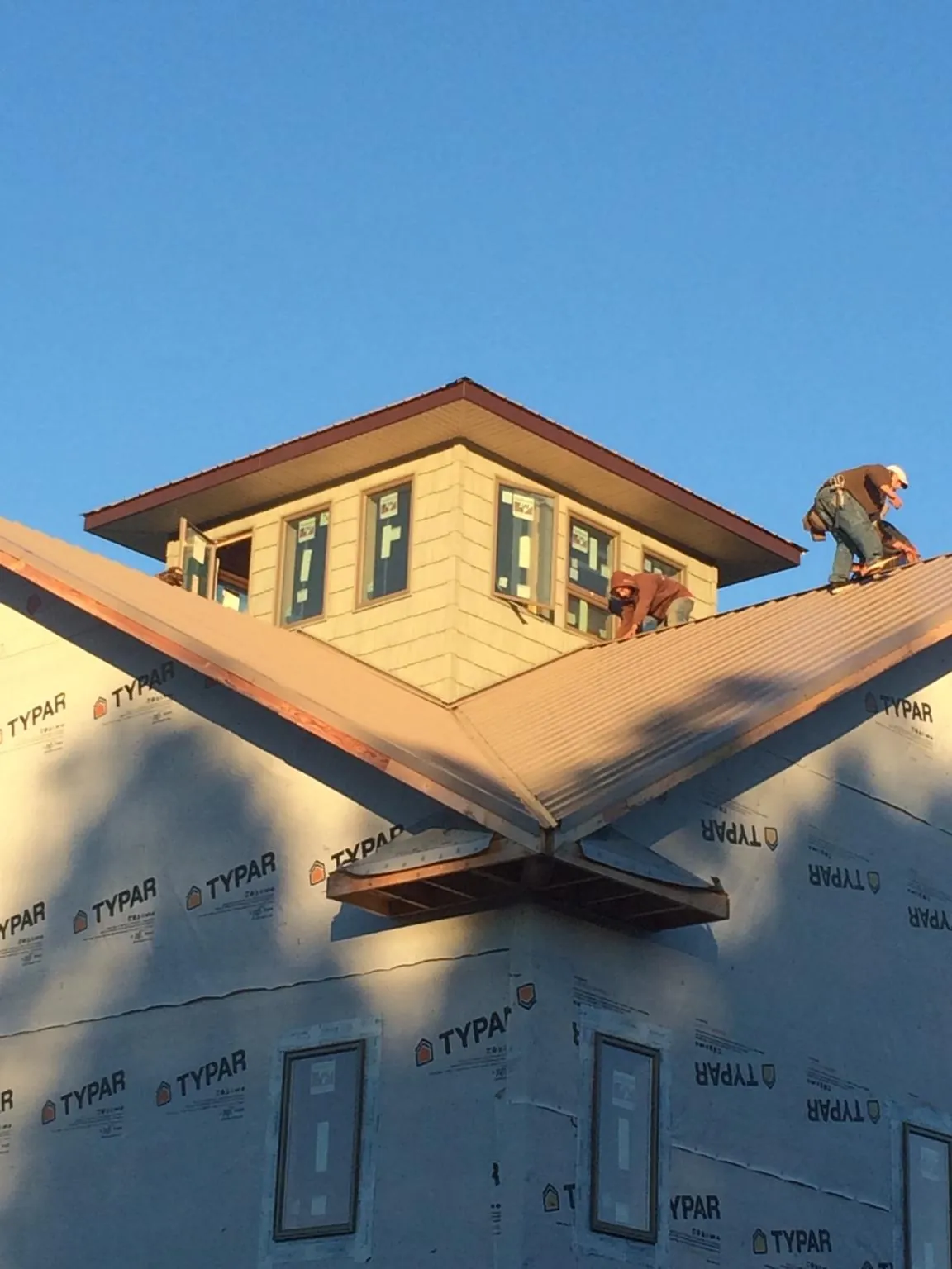 Roofers working around a rooftop cupola on a new metal roof at sunset — Roof Waterproofing in Oakland Gardens by Roofing Brothers